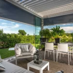 Pergola bioclimatica KE in giardino con piante e salotto da esterno